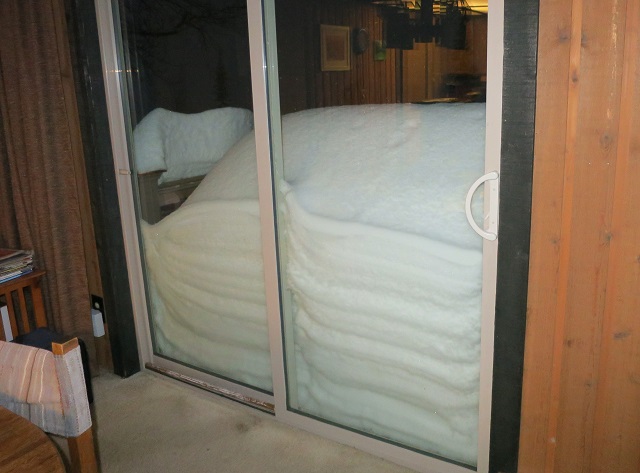 Snow piled up next to a sliding glass door viewed from inside