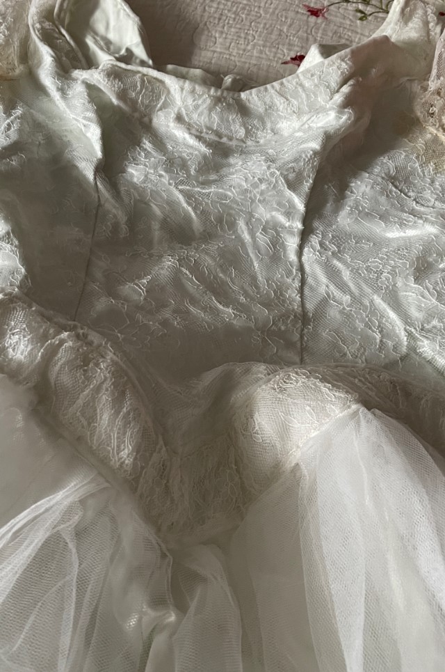 Closeup of a wedding dress laid out on a bed showing the bodice and part of the skirt.