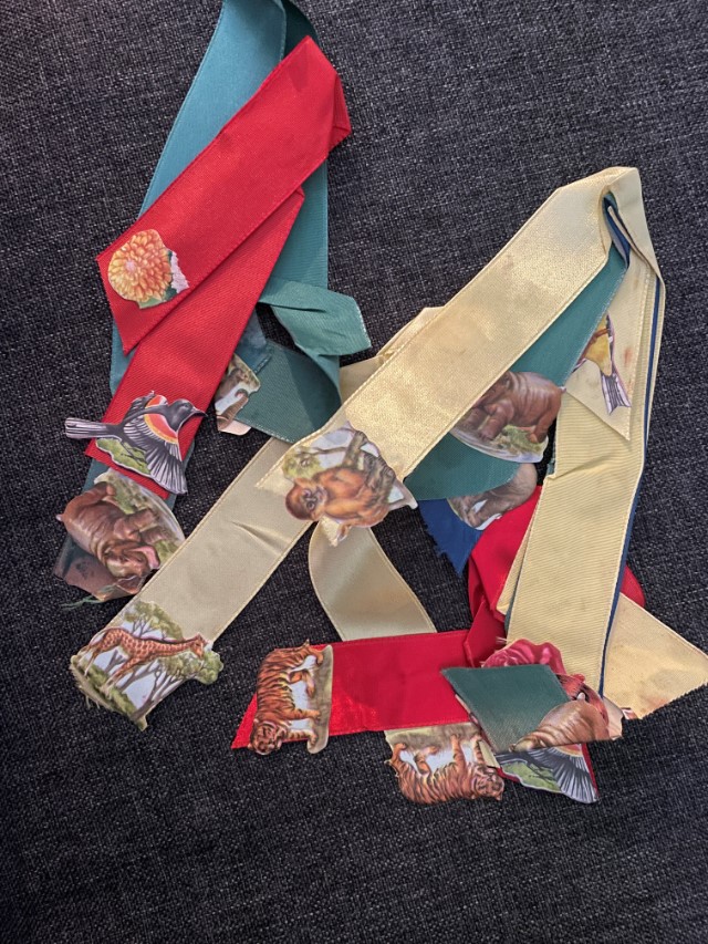 Wide satin ribbons in red, green, yellow, and blue, folded in half, with animal stickers affixed near the ends. Animals include tigers, giraffes, monkeys, hippos, birds, and one flower which I just noticed as I was writing this alt text.