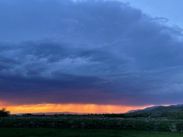 Sunset scene dominated by a moody cloudy blue sky that takes up about four-fifths of the frame. There's a band of yellow and orange sandwiched between the clouds and the darker landscape below.