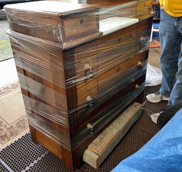 Warm brown wooden dresser wrapped in plastic cling film and sitting on a dolly.