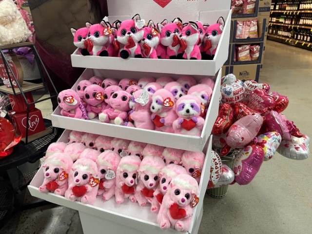 Store display with three shelves of pink stuffed animals holding hearts: foxes, turtles, sloths, and hedgehogs (I think).