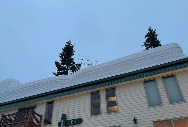 Flat roof of a condo building piled with several feet of snow in layers.