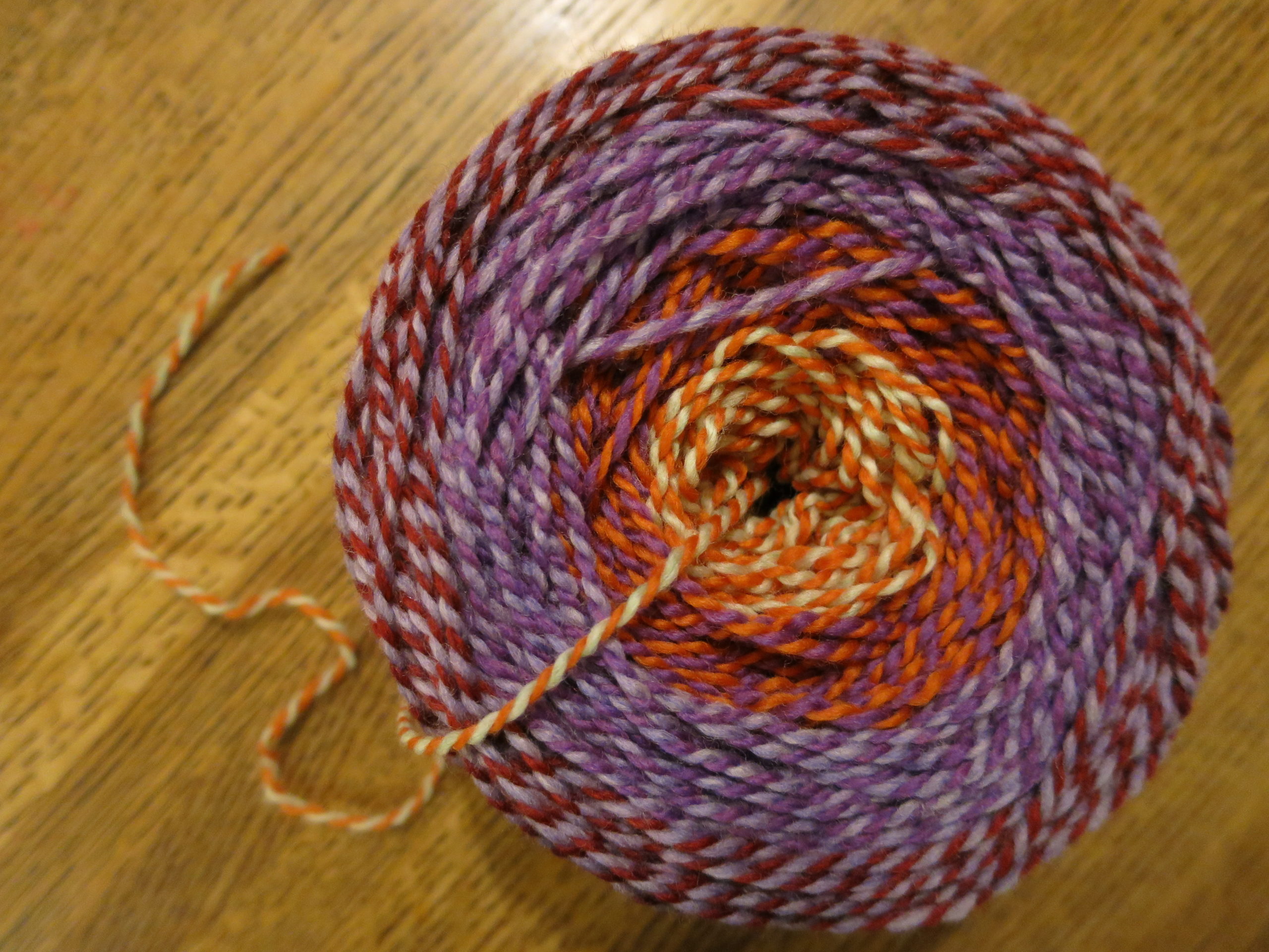 cake of multicolored yarn in purples, orange, dark red, and tan